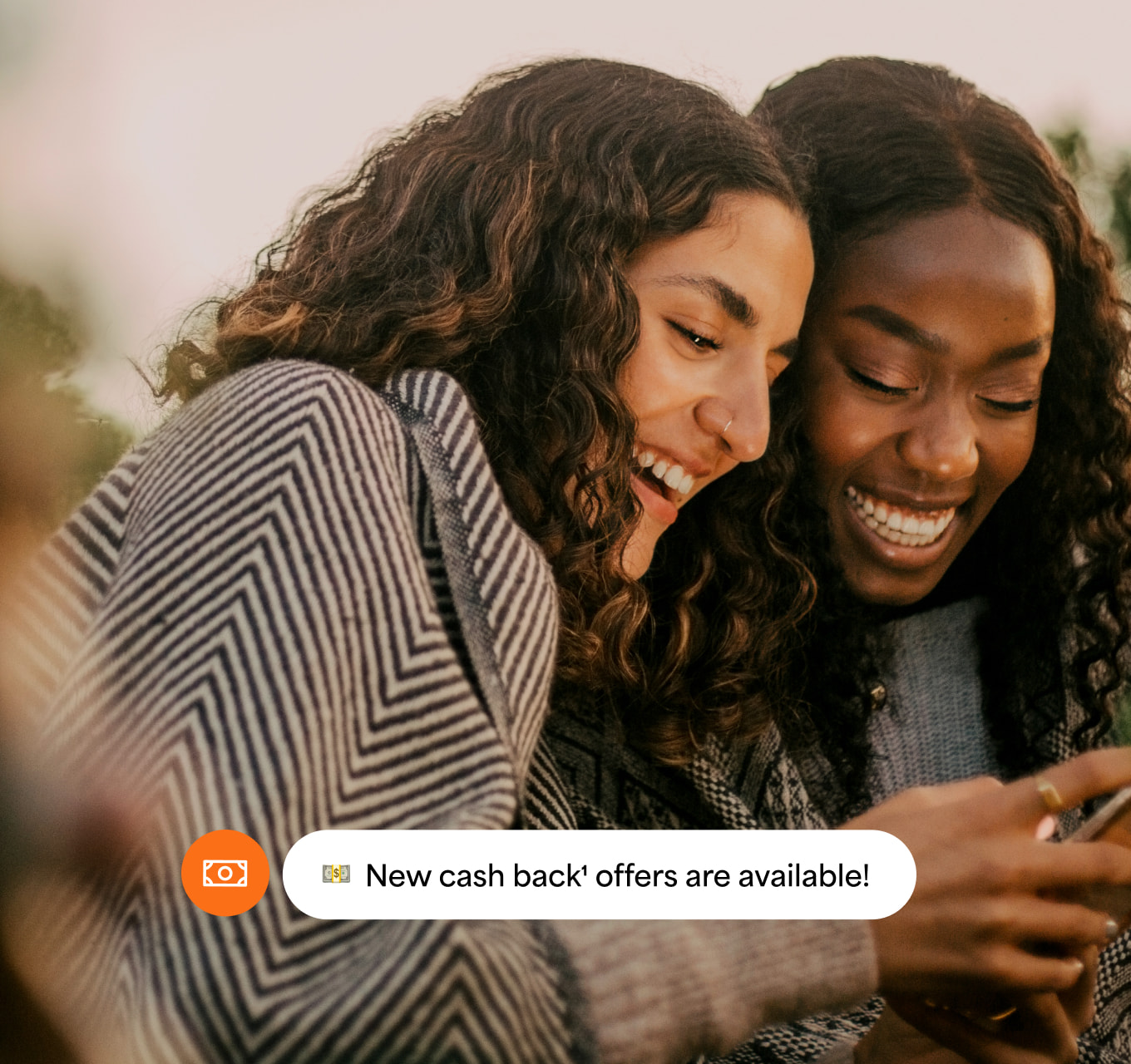 Two women looking at their phone with a cash back offers notification.