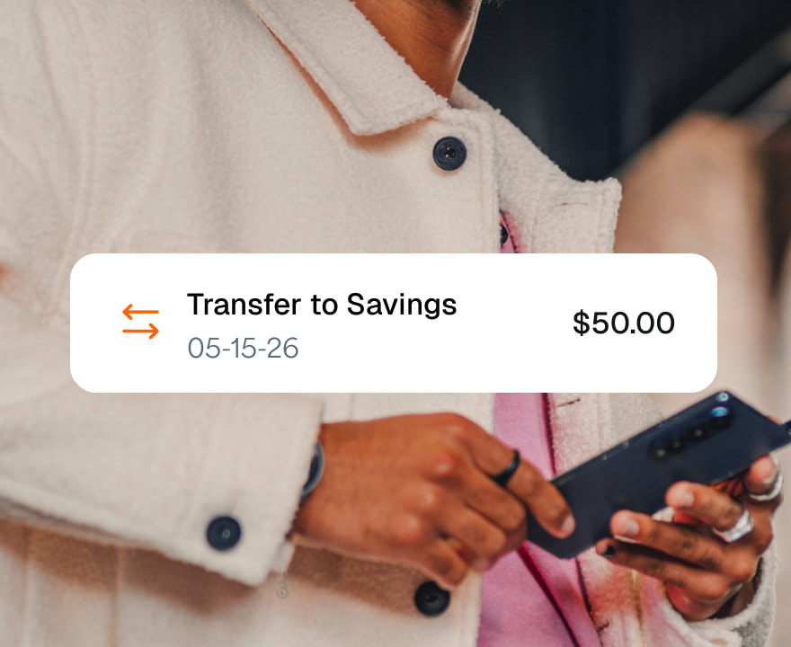 Someone holding a phone with a notification of a $50 transfer to savings